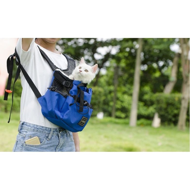 Person carrying a white cat in a blue bag outdoors, with green trees in the background.