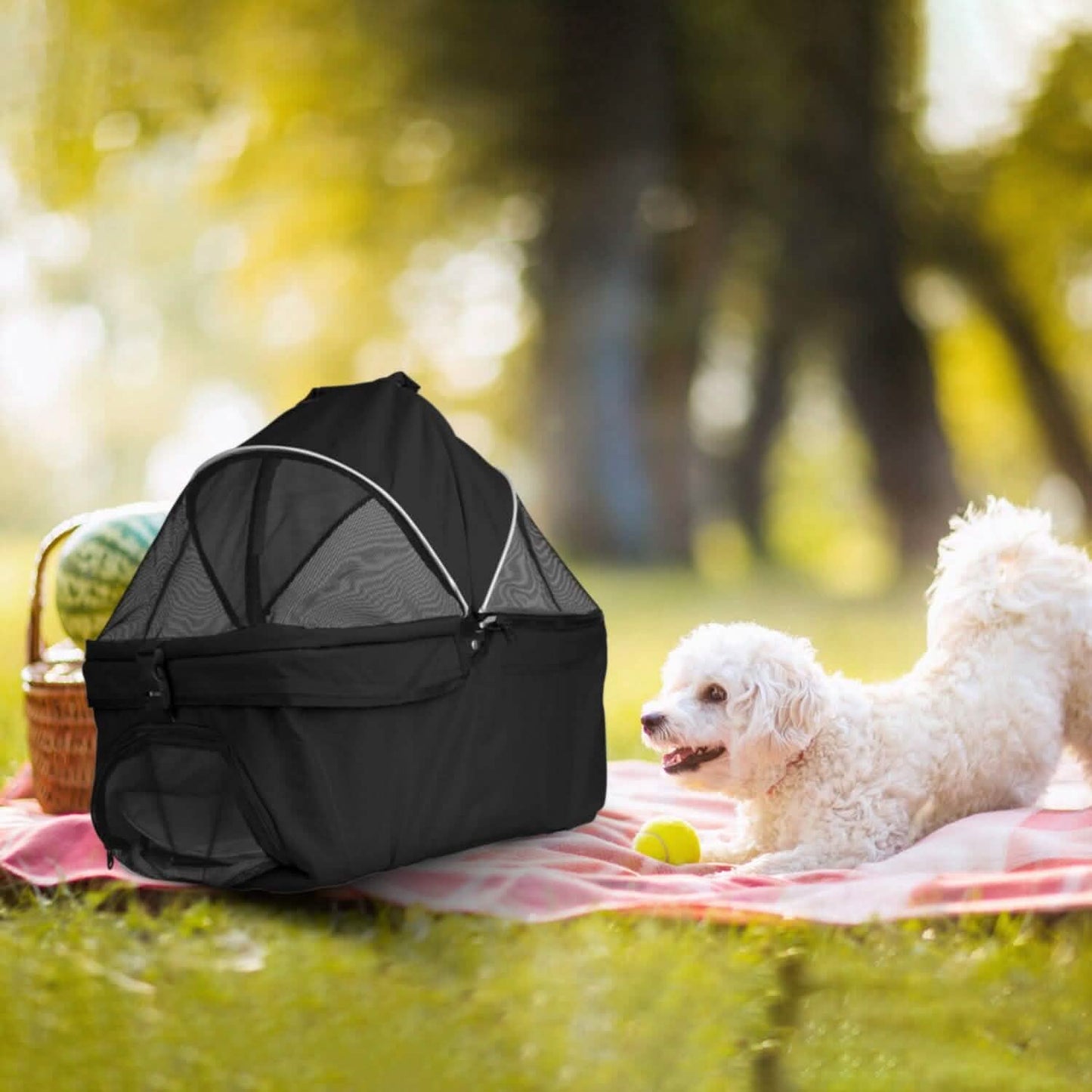 White dog on pink blanket with black pet carrier and basket in sunny park.