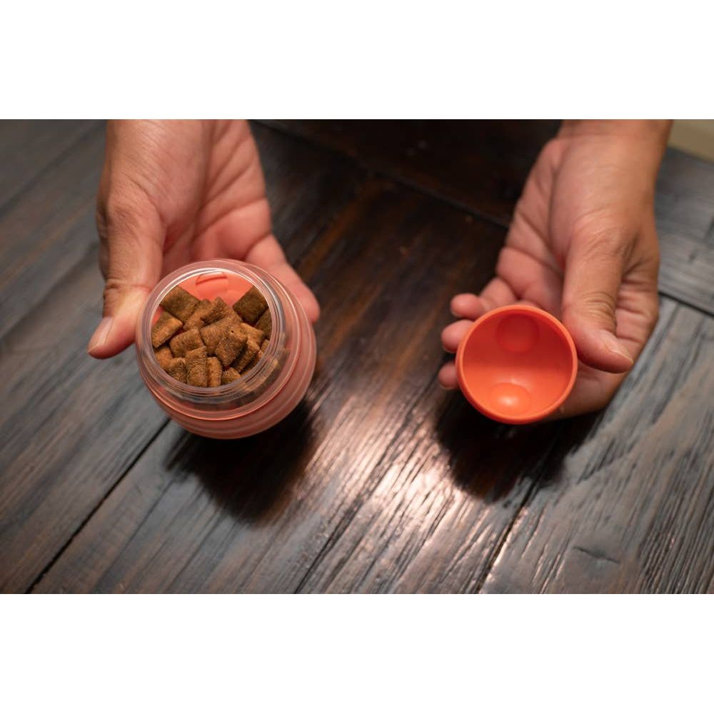 Hands holding an open jar with brown pellets and an orange lid on a wooden table.