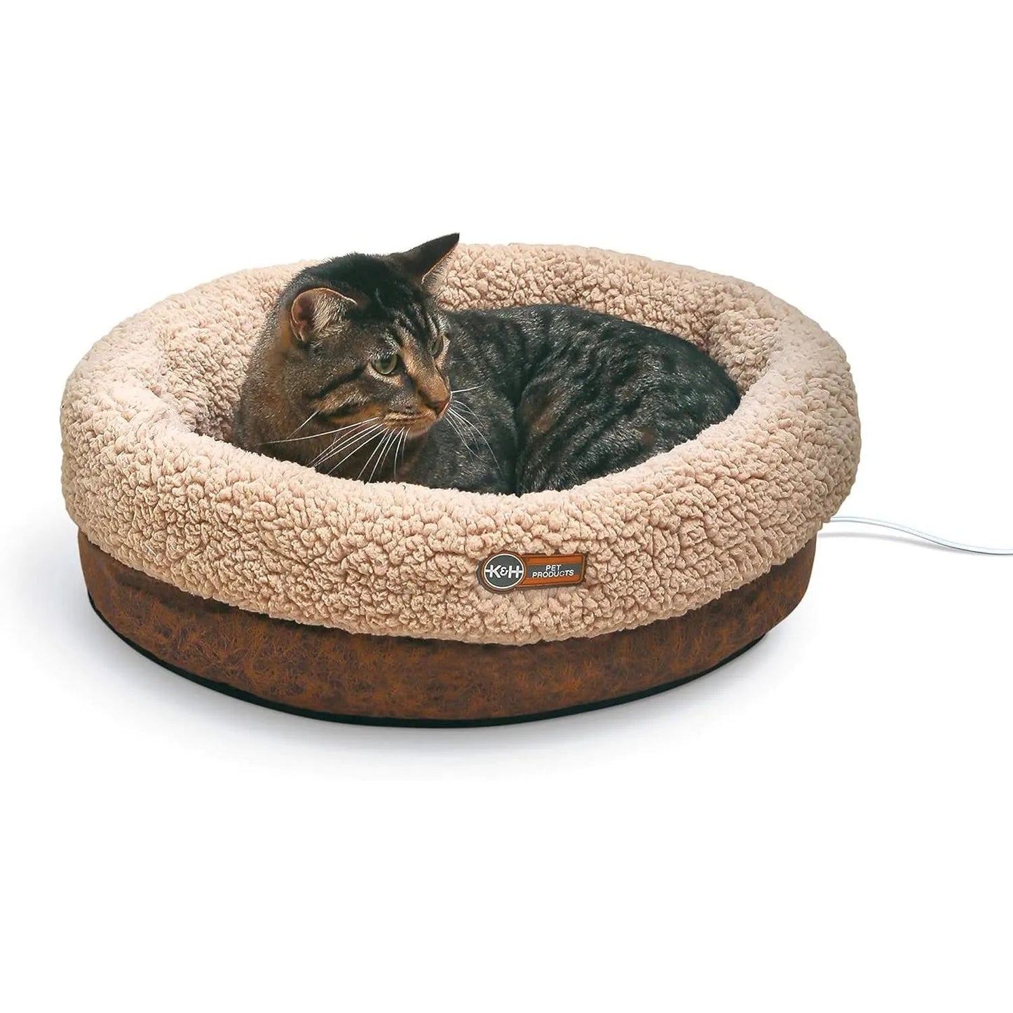 Tabby cat lounging in a round, beige, plush pet bed with a brown base and a visible power cord.