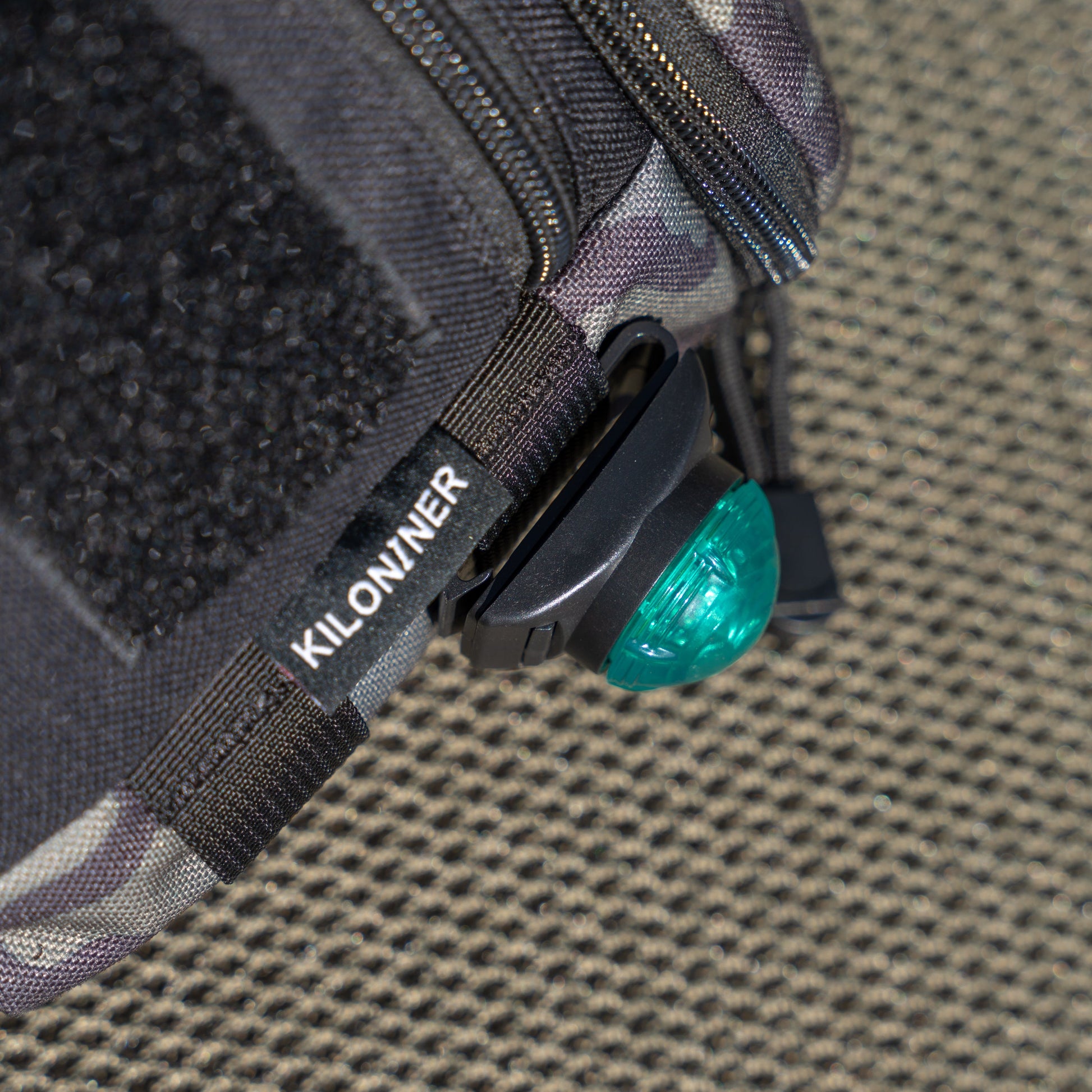 Close-up of a black bag corner with a green light and "KILONINER" label on a textured surface.