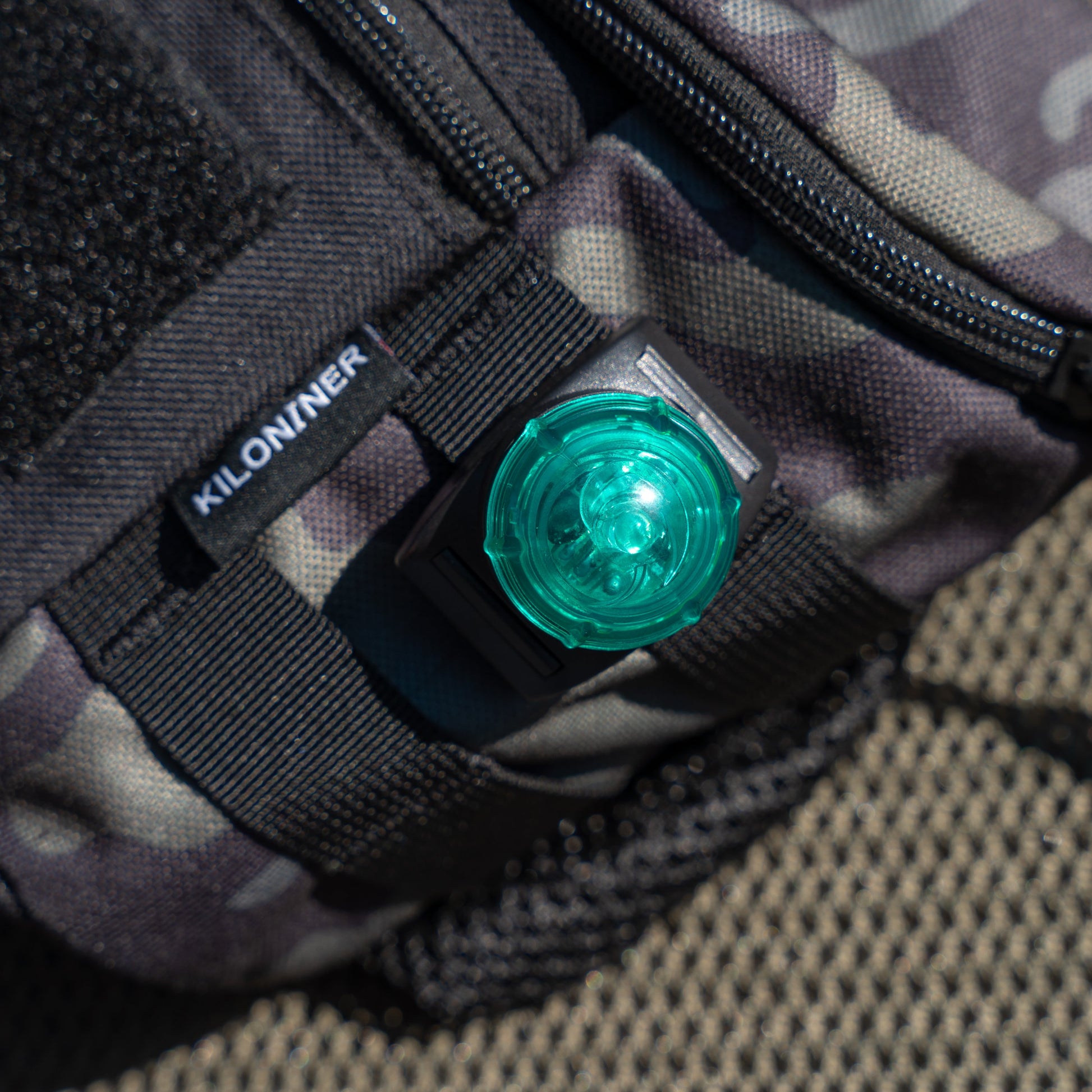 Black bag with a green light attached, featuring a "KILONINER" label and camouflage pattern.
