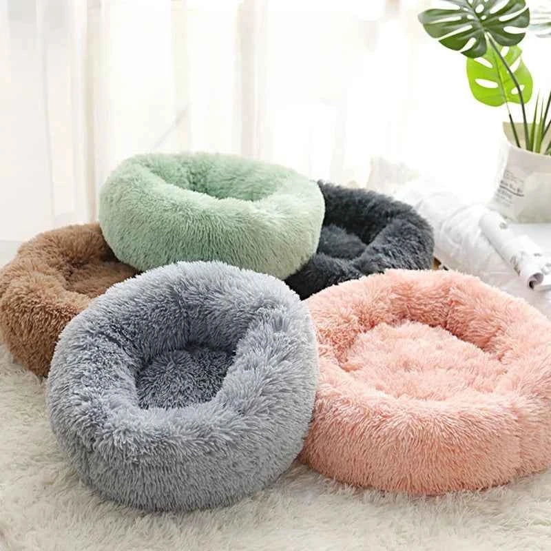 Five fluffy pet beds in pastel colors: green, black, brown, gray, and pink, on a white rug.