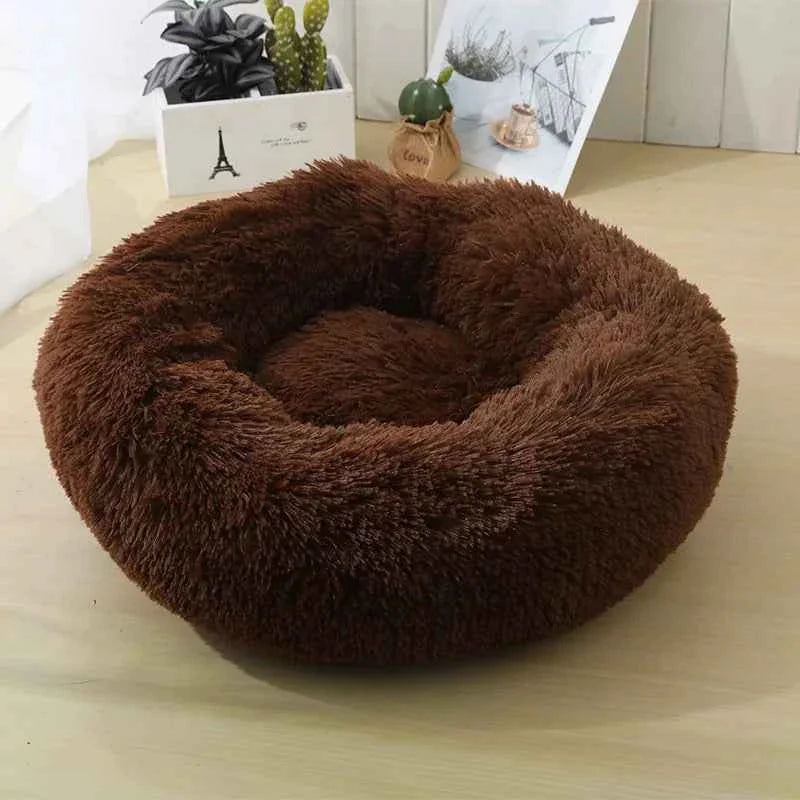 Fluffy brown pet bed on a wooden floor, with decor and plants in the background.