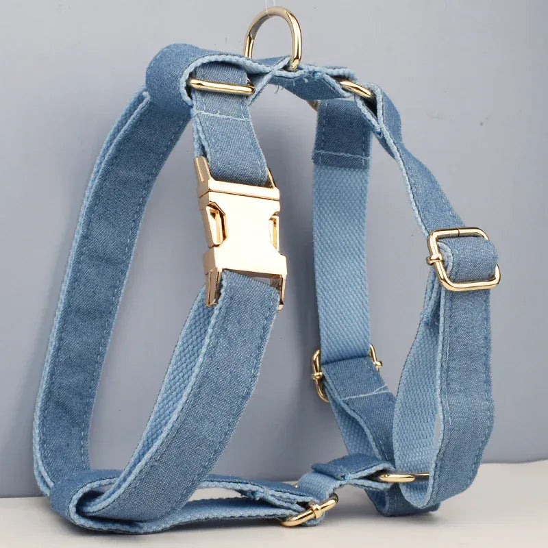 Blue denim dog harness with gold metal buckles and a ring, set against a light gray background.